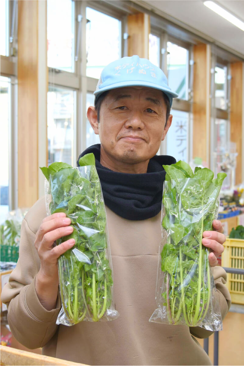 採れたての小松菜やルッコラを掲げる山上信一さん